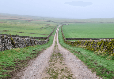A stony farm track between two stone walls leads into the mist ahead.