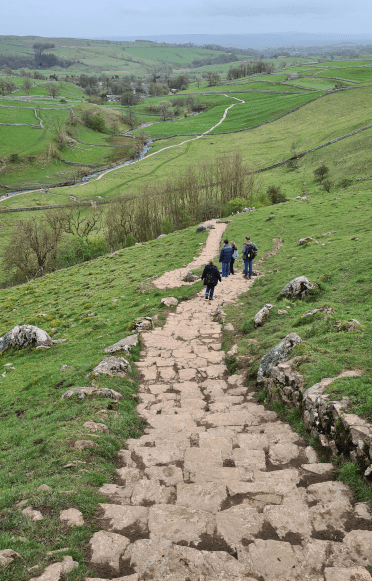The knobbly stone path that leads up to the top of Malham Cove. Walkers descend it, with stunning views of the green valley below.