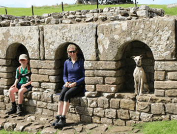 A parent, child and dog each sit in an alcove in the wall of a Roman Fort on Hadrian's Wall Path.