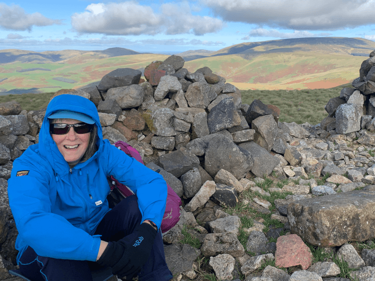 A tired but exuberant walker takes a well-deserved break after a steep climb on the Pennine Way, sheltering behind loosely stacked rocks with far-reaching views over the exposed moorland beyond.
