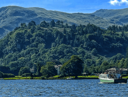 A boat crosses the waters of a lake beneath Lake District mountain peaks.