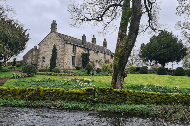 A great example of the architecture in Yorkshire: a pale stone house nestles amongst the trees beside the river rushing in the foreground.
