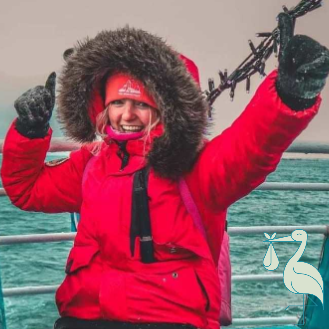 Hayley H, tour pack administrator and GDPR office, sits on a boat in arctic waters wearing a red hooded parka.