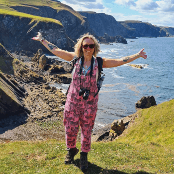 Angie, tour operations administrator at Contours Holidays, stands with arms outstretched in brilliant sunshine on a coastal walk.