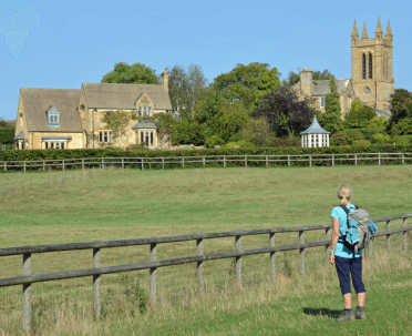 A walker looks across a field to a town in the Cotswolds.