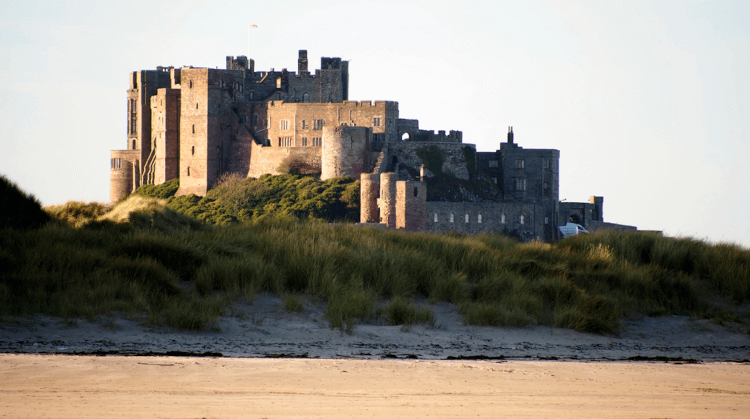 Bamburgh Castle, a huge and very complete castle rising out of the dunes as viewed from a sandy beach on the coast of Northumberland.