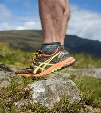 Preparing to climb steep fell slopes, a prospective runner strengthens their calf muscles by rising to their tiptoes on a rock.