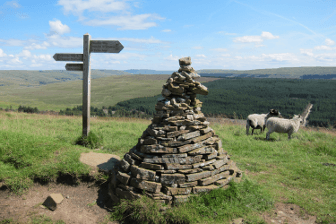 A large, neatly built cairn sits at the top of Cam High Road on the Pennine Way, with far-reaching views over the springtime countryside below.