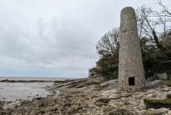 A stone chimney stands on a rocky beach.