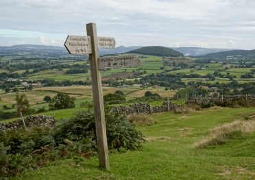 A waymarker for the Cleveland Way stands above a patchwork quilt of green fields.
