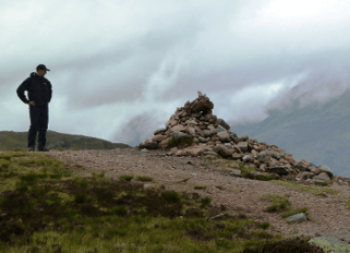 A man stands by a cairn atop a stony peak on the West Highland Way walking holiday.