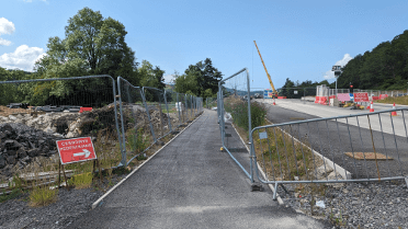 During road works, the pedestrian footpath on this slow way is diverted between metal fences by a red sign.