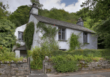 Vines and other greenery shroud the small grey shape of Dove Cottage, once home to William Wordsworth.