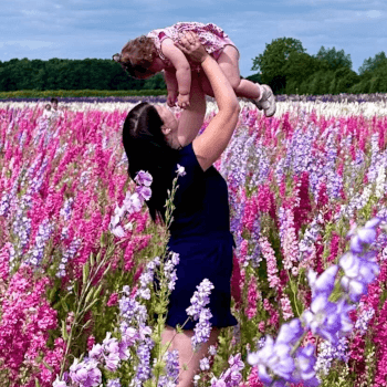Emma, out-of-hours customer services advisor, lifts her child above her head in a field of flowers.