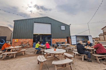 Walkers sit at tables drinking beer in front of a green metal barn.