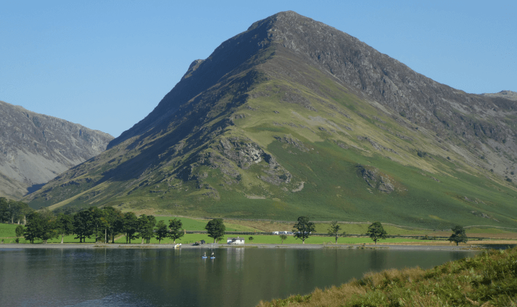 Views over Buttermere from the flat circular walking path to Fleetwith Pike, a large rocky fell rising above the clear, still water.