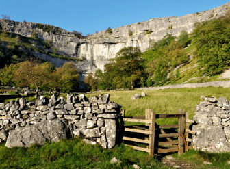 A wooden gate stands ahead of the limestone cliff-face at Malham.
