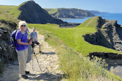 Two walkers enjoy a sunny day out on the South West Coast Path with Contours Holidays, an experience you could discount for a friend or family member with a Contours gift voucher.
