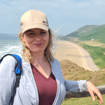 Gosia, database team manager, out in the UK countryside with the sea and a sandy beach behind her.