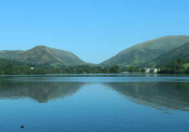 A photo taken across the still waters of Grasmere to the lumpy Lake District hills beyond.