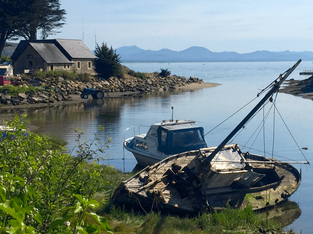 A boat lies on the beach with a house and the ocean in the background, as seen on the Llyn Coast Path.