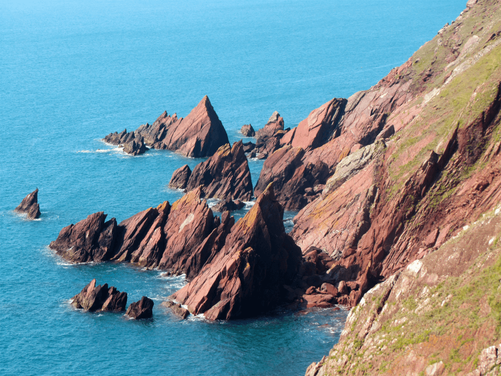 Sharp reddish rock stabs upward through the surf on the Pembrokeshire Coast Path holiday.