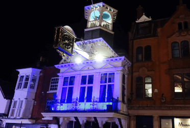 Bright blue light illuminates the storefronts of Guildford at night.