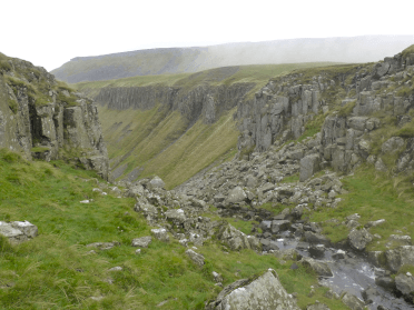 Views over low-lying vegetation to the exposed rocks and great glaciated chasm of High Cup Nick, one of the most inspirational sights on the Pennine Way.