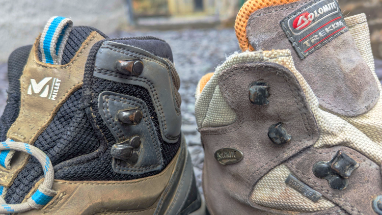 A pair of Millet hiking boots and a pair of Dolomite trekking boots sit together with the focus on the metal hooks at the top of the shoe.