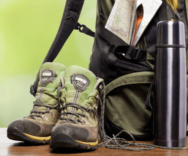 Essential hiking equipment: a pair of hiking boots sits next to a rucksack and a thermos.