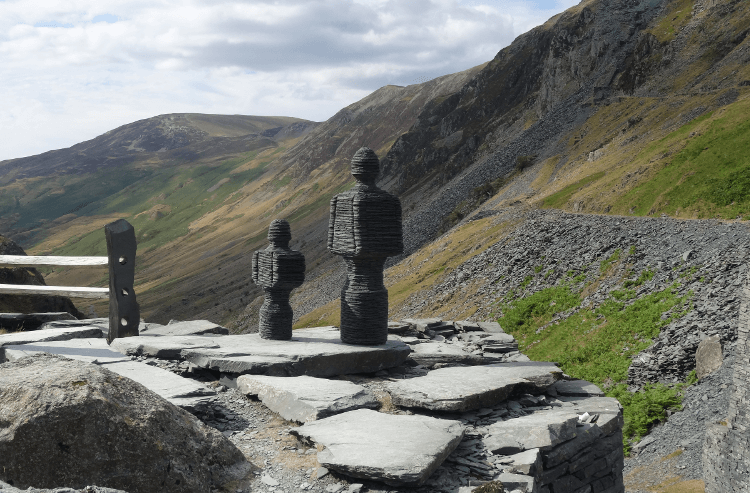 A slate statue sits in front of a mountainous backdrop at Honister Pass.
