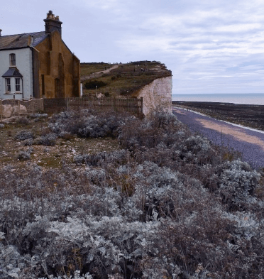 A house sits atop the cliffs at Seven Sisters, with views down to the sea behind.