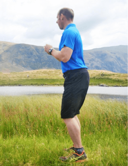 A man prepares to climb the fells with squat exercises, beginning with this upright pose.