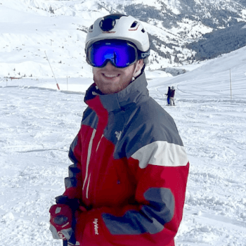 Isaac, database administrator at Contours Holidays, standing on a ski slope in red ski gear.