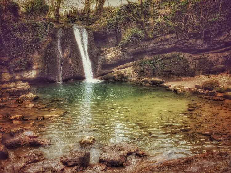 A waterfall pours into a secluded, rocky pool at Janet's Foss in Yorkshire.