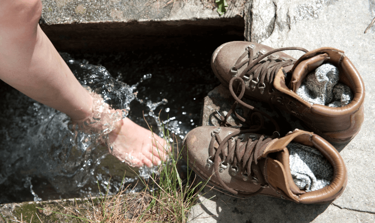 A walker removes her boots to rinse and cool her feet in cold clean water.