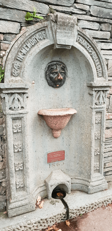 An ornate stone fountain in Keswick, with a worn metal lion's head mounted in the middle and a dedication to Frances Rolleston.