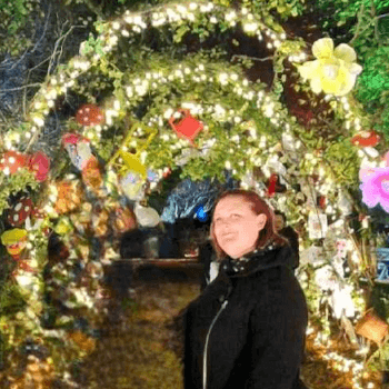 Melody, marketing and social media manager, stands in front of a fairy light arch at night.