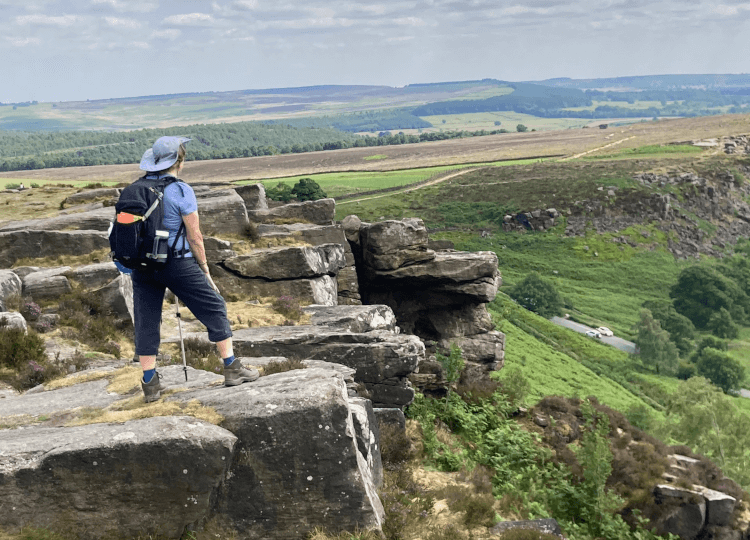 From a projecting shelf of rock, a walker looks out over the landscapes of the Peak District.