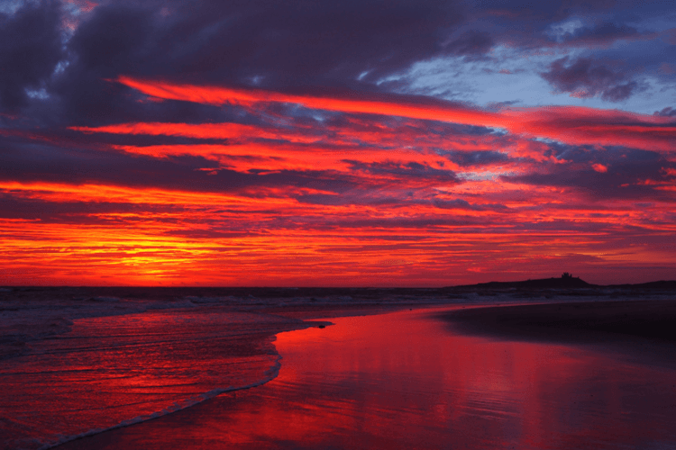 A vibrant red sunrise on a beach in Northumberland.