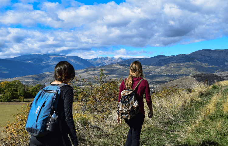 Two women rambling along a grassy track beneath distant mountains, with plenty to be nosey about along the way.