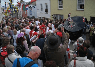 The narrow streets of Padstow are criss-crossed with bunting and bustling with a huge crowd, all eyes on the Obby Oss as it makes its way through town.