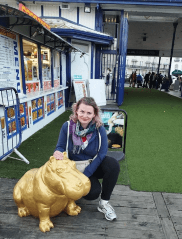 Gosia sits beside a golden hippopotomus statue on Eastbourne Pier.