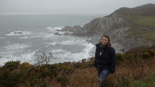 Gosia stands in the foreground as the waves crash against the rocks below.