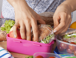 A beginner walker prepares a packed lunch for their hike, placing sandwiches safely into tupperware dishes so they don't get crushed.