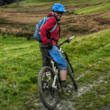 Richard, senior customer services advisor, sits on his mountain bike in a green field on the Trans Cambrian Way.
