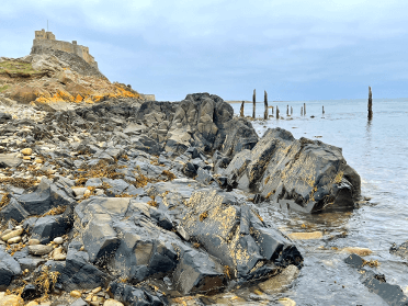 Lindisfarne looms in the background as water laps at the rocks on the causeway.