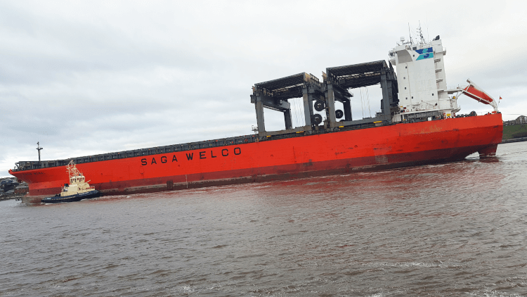 An enormous red cargo ship floats off the shores of the Northumberland Coast.