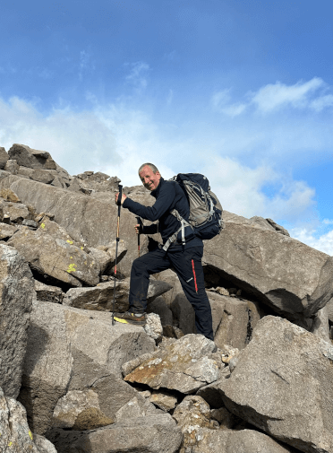 A walker poses halfway up a rocky scramble on the Bob Graham Round.