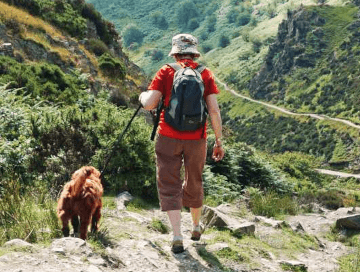 A walker prepares to descend a rocky hill on a walking holiday with her dog, a red spaniel mix.
